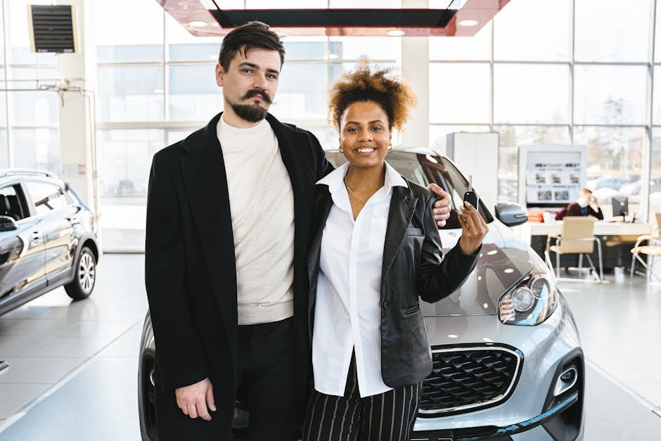 Interracial couple celebrates buying a new car at a dealership, holding keys and smiling.